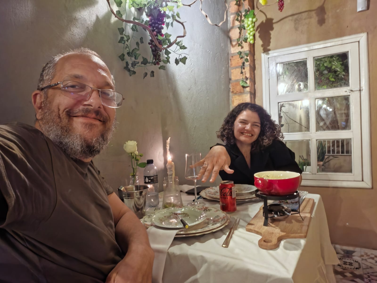 Juliana mostrando a aliança no dedo, sorrindo à mesa do jantar com Lucas